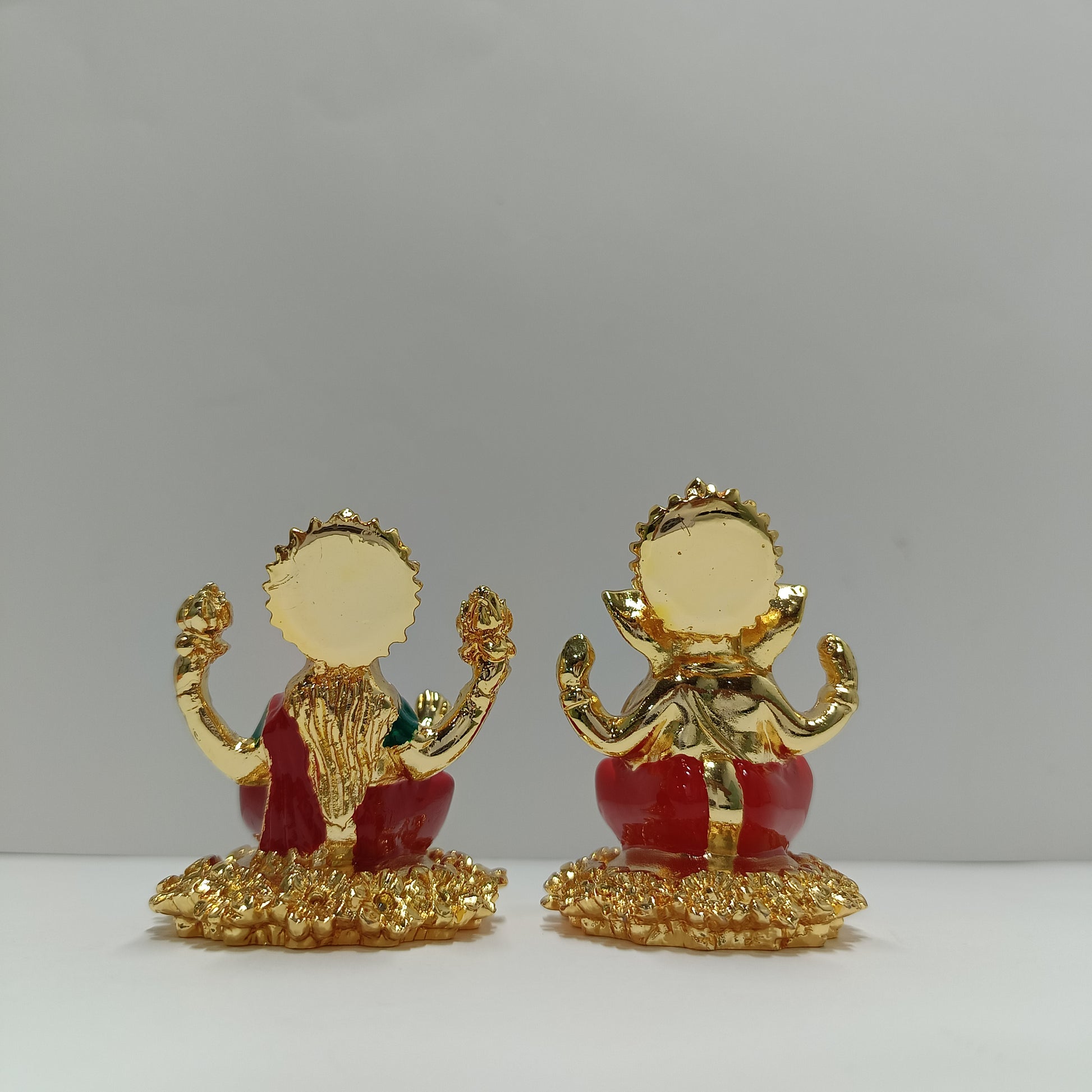 Two golden idols of Hindu deities Ganesha and Lakshmi sitting side-by-side on a light background.