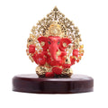 A red and gold Ganesha idol with a golden, leaf-patterned halo (Kalpavriksha tree design) seated on a dark wooden base.