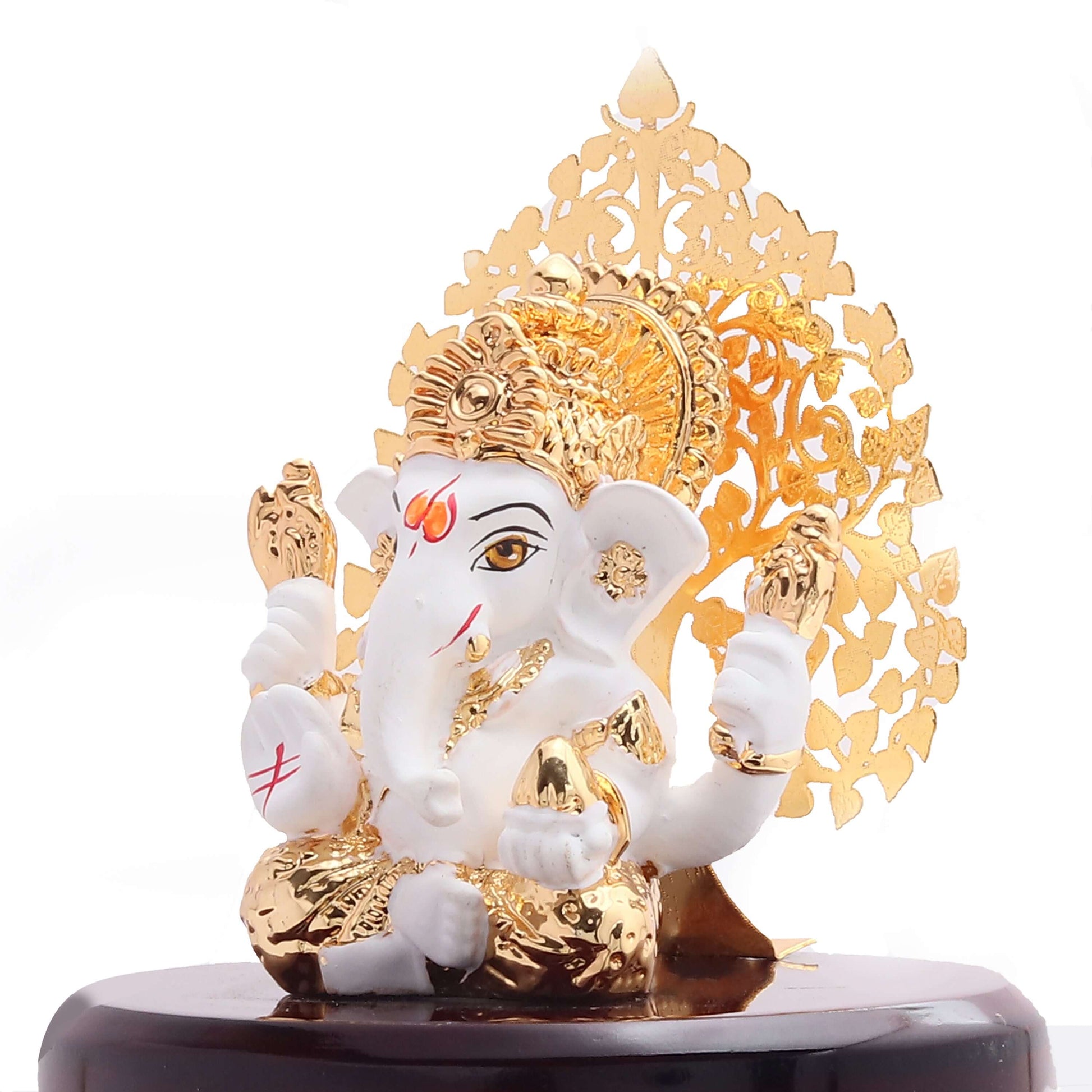 White and gold Ganesha idol sitting on a dark wooden base with a golden, intricate backdrop.
