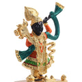 A close-up of a gold-plated, multicolored statue of Lord Shreenath Ji, a form of Lord Krishna, standing with an arm raised and adorned with intricate details and a green scarf.