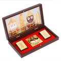 A polished wooden box frame, open to reveal gold-plated figurines of Lord Jagannath, Lord Balabhadra, and Devi Subhadra on the left, and a pair of gold-plated Charan Padukas (sacred footprints) on a red base on the right. Two small, inscribed golden plaques are also visible, one on each side of the Padukas