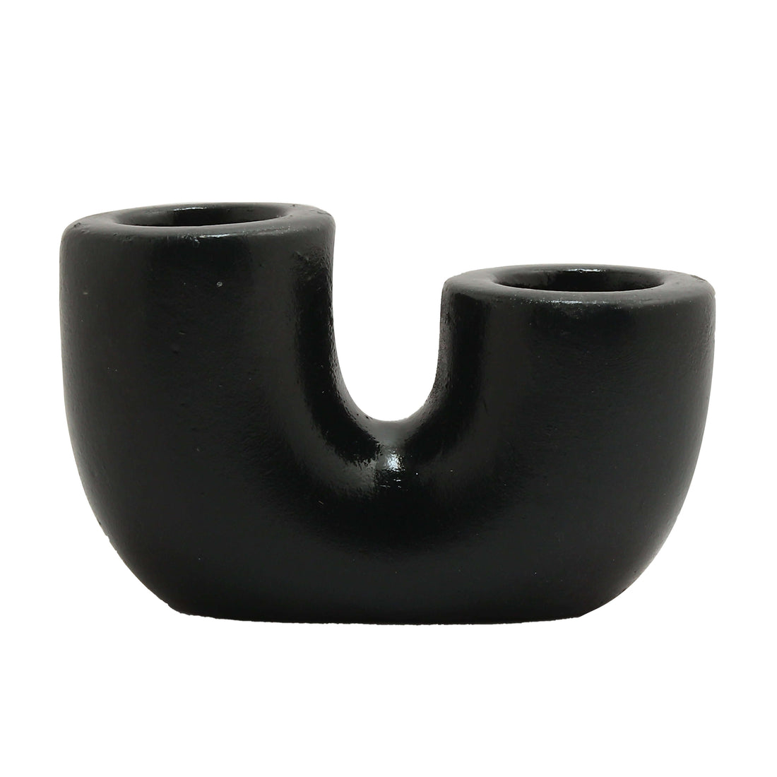 A black U-shaped candle holder with two lit candles placed on it, set against a neutral background with a plant to the side.