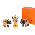 A gold-plated Balaji idol in black, flanked by two black and gold elephant statues, with an orange gift box featuring the 'WEMY' logo in the background.