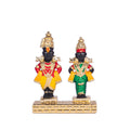 A black statue of Vitthal in a yellow and red dhoti stands next to a black statue of Rukmini in a green and gold sari, both adorned with gold jewelry and placed on a golden base.