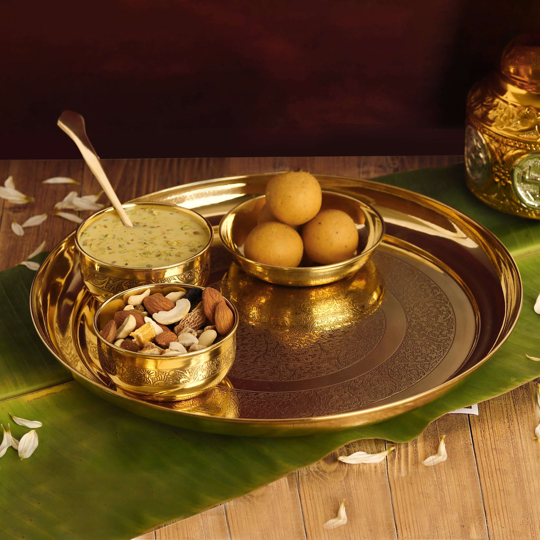 A traditional Indian Bhog Thali set with a golden platter, three bowls, and a spoon, presented with food offerings.