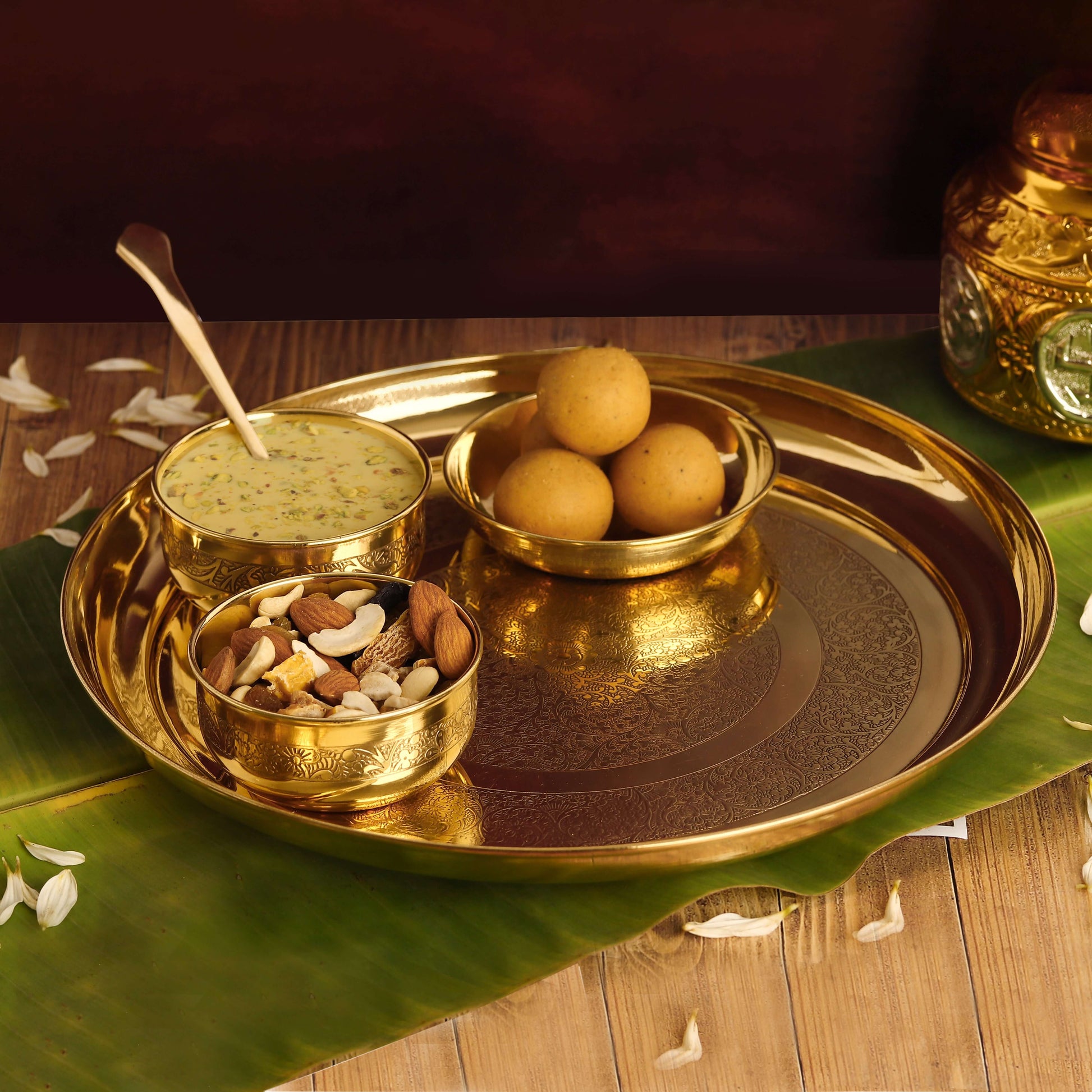 A traditional Indian Bhog Thali set with a golden platter, three bowls, and a spoon, presented with food offerings.