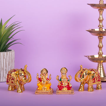 Gold and red idols of Lord Ganesha and Goddess Lakshmi sit centrally on a purple surface, flanked by two ornate elephant statues, with a potted plant on the left and a traditional tiered brass lamp on the right, against a light purple background.