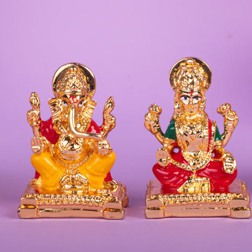 Golden statues of Lord Ganesha and Goddess Lakshmi on a purple background.