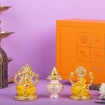 Golden idols of Lord Ganesha and Goddess Lakshmi with a decorative crystal kalash in between, placed in front of an orange gift box with traditional Indian symbols, on a purple background.