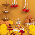 A gold-colored Swami Samarth idol seated on a base, surrounded by yellow and red flowers, brass peacock diyas, and laddoos, set against a warm yellow background.