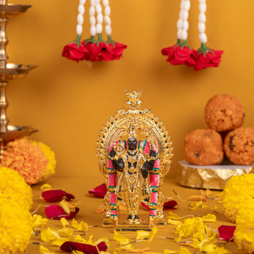 Golden colored idol of Lord Murugan (Kartikeya/Subrahmanya) standing on a decorative base, adorned with pink and green accents, surrounded by offerings of yellow marigold flowers, red rose petals, pearl garlands with red roses, and a stack of Indian sweet laddus on a gold background.