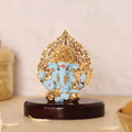 A light blue Ganesha idol with gold accents, and a detailed gold Kalpavriksha Tree halo, is shown seated on a glossy dark wooden base. The idol is approximately 3 inches in height.