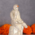 A white, luminous idol of Shree Sai Baba seated in a blessing posture, with an orange mark on his forehead.