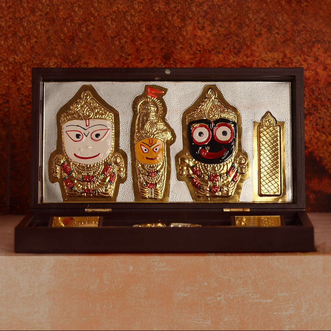 Open wooden box showcasing gold-plated Lord Jagannath idols and religious items, including padukas, on a red lining.