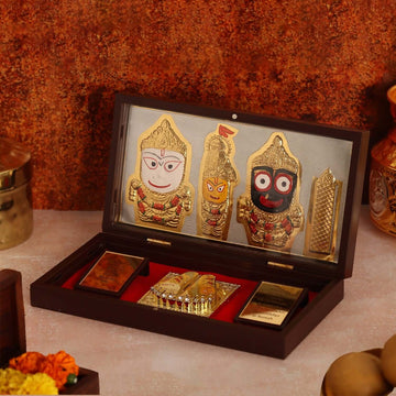 Open wooden box showcasing gold-plated Lord Jagannath idols and religious items, including padukas, on a red lining.
