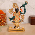 A meticulously crafted idol of Lord Shreenath Ji (a form of Lord Krishna) standing upright, adorned with intricate golden ornaments and vibrant green and orange garments, on a golden base. The idol features dark skin, a prominent nose, and large, expressive eyes, with one arm raised and the other holding a staff or a collection of flowers. The overall impression is one of divine beauty and reverence.