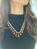 A woman wearing a black top and a V-shaped necklace with Orange shaded beads and gold accents.