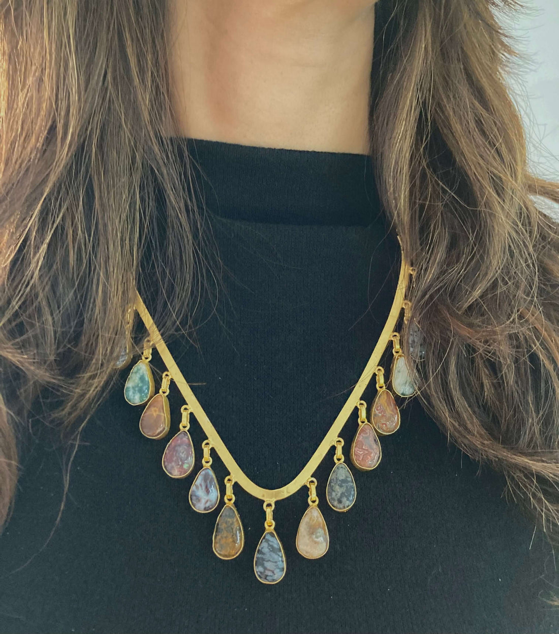 A woman wearing a black top and a V-shaped necklace with blue beads and gold accents.