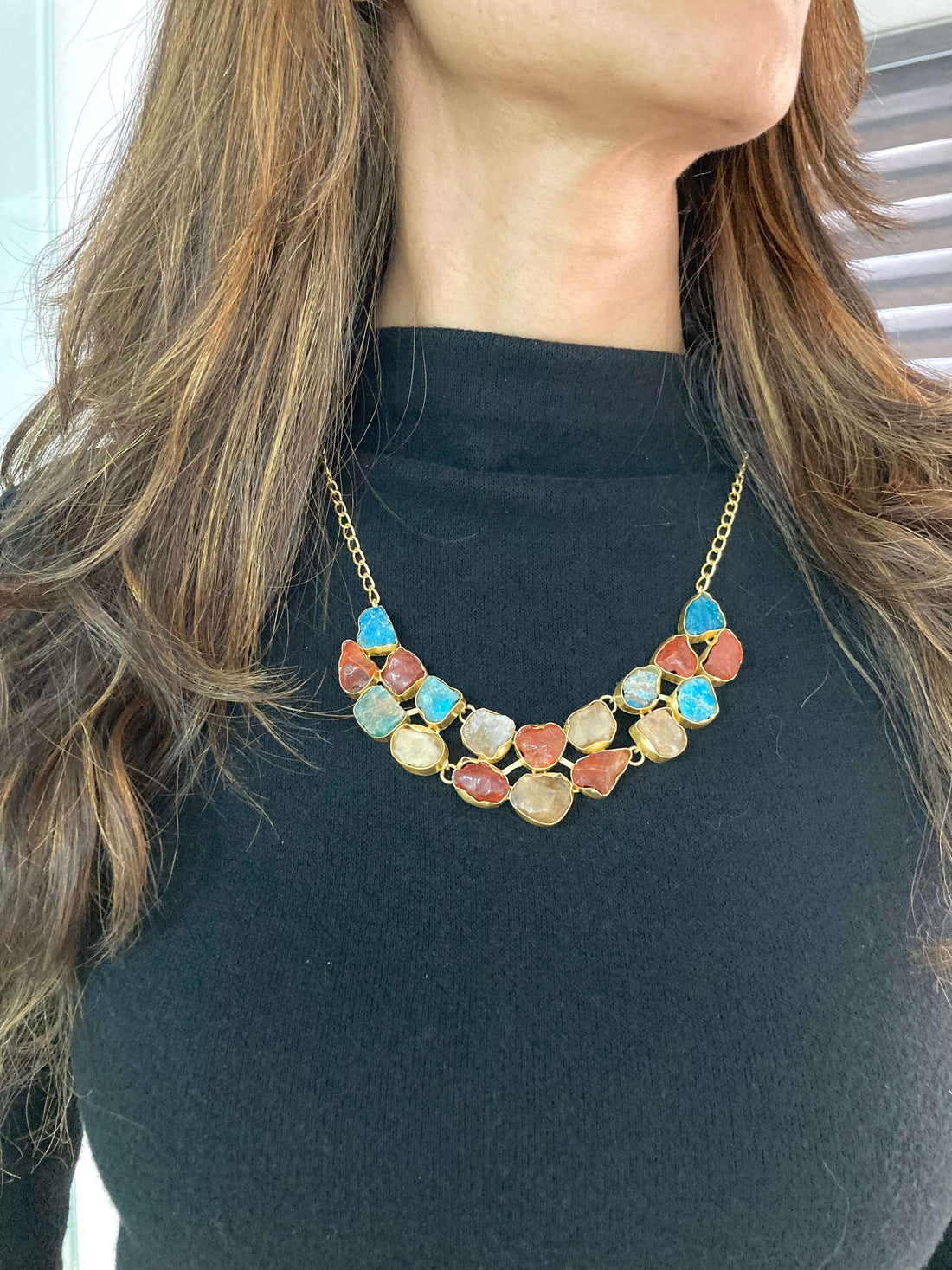 A woman wearing a black top and a layered necklace with beige and brown beads.