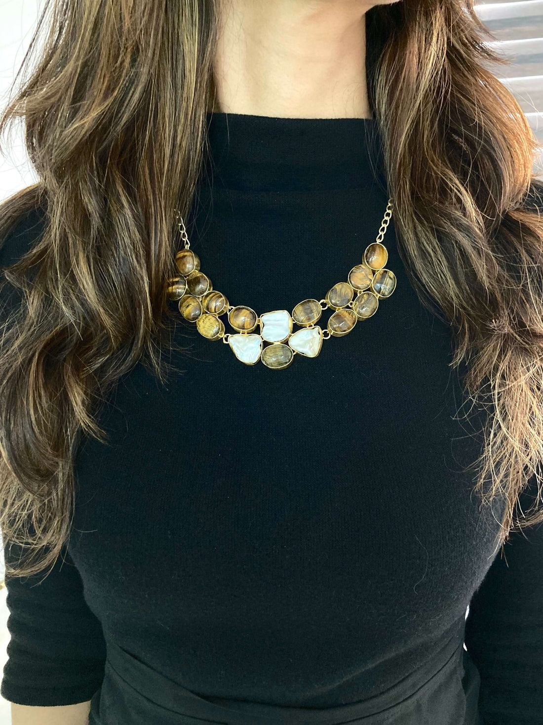 A woman wearing a black top and a layered necklace with beige and brown beads.