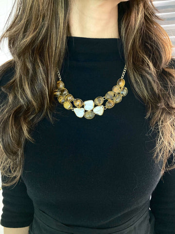 A woman wearing a black top and a layered necklace with beige and brown beads.