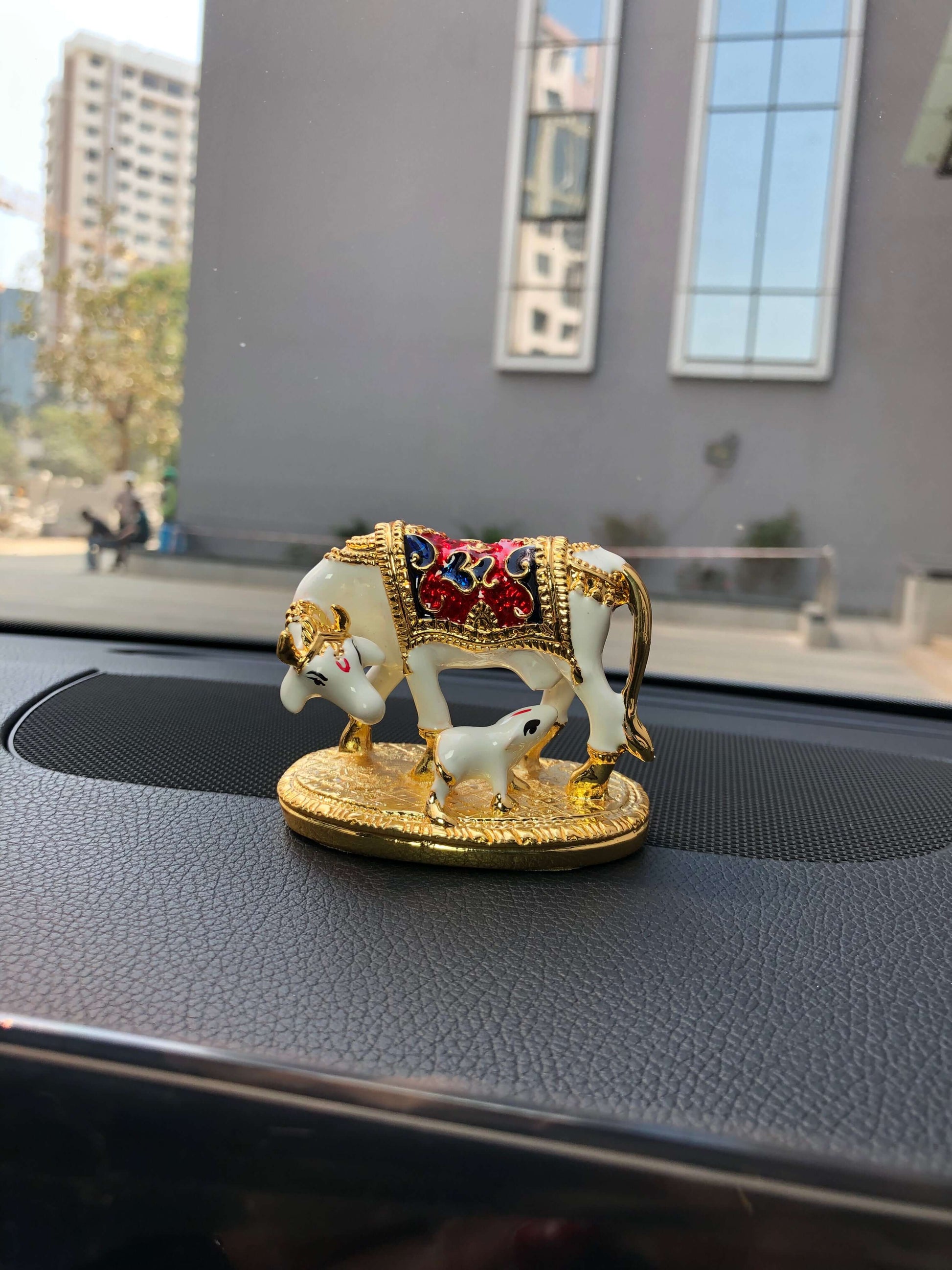 Golden Kamadhenu cow and calf idol with colorful accents displayed on a car dashboard.