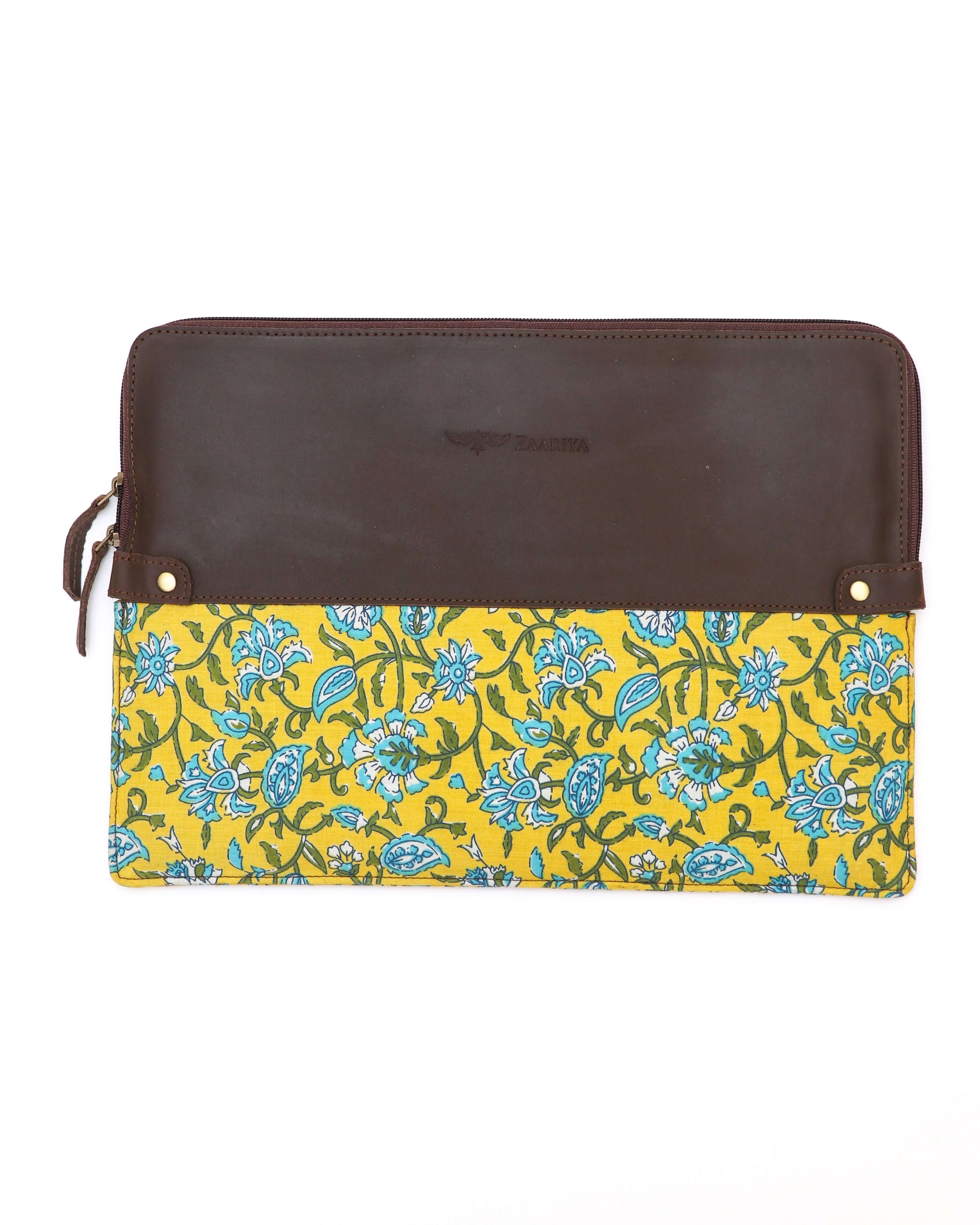 A leather laptop sleeve with a yellow floral block print on the lower half and a solid brown upper half, zipped closed.