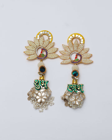 A pair of decorative Shubh Labh door hangings, featuring a beaded lotus design with a small peacock motif and a circular yellow backing. Below the lotus, a dangling silver bell-shaped piece is decorated with a green text "शुभ" and "लाभ" respectively, and small pearls hanging from the bottom.