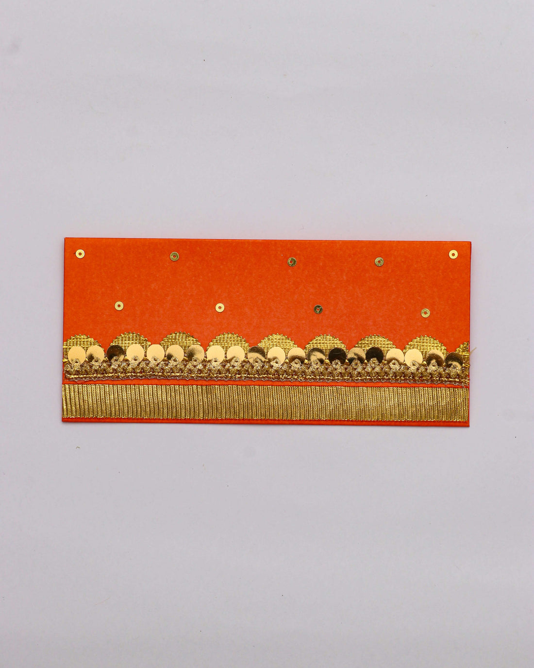 An orange Shagun envelope with gold and black embellished trim and a fringe of gold thread along the bottom. The envelope is also decorated with small gold sequins scattered across the top half.