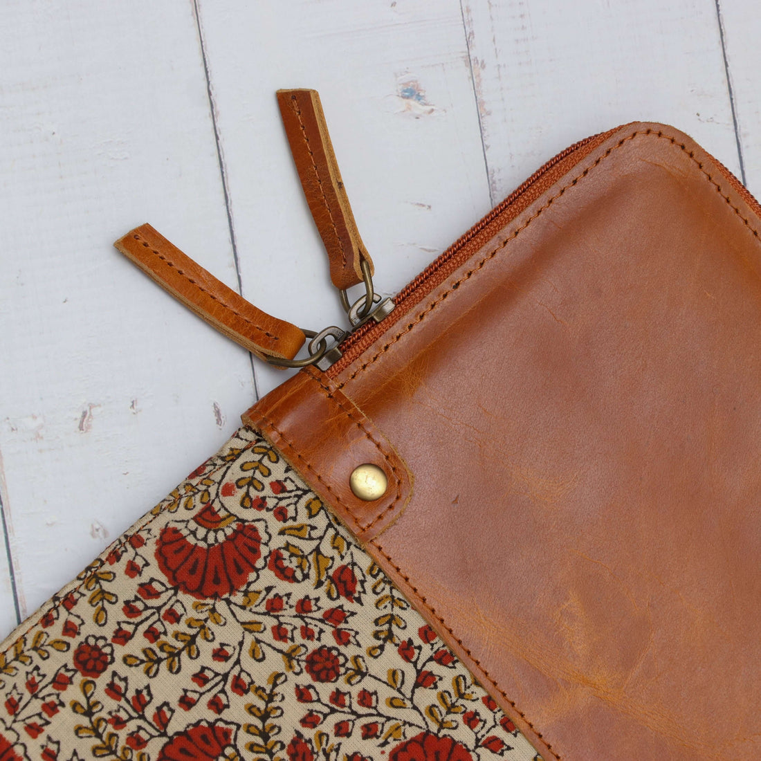 A brown leather laptop sleeve with floral block print design, displayed alongside a white laptop and a computer mouse on a wooden surface.