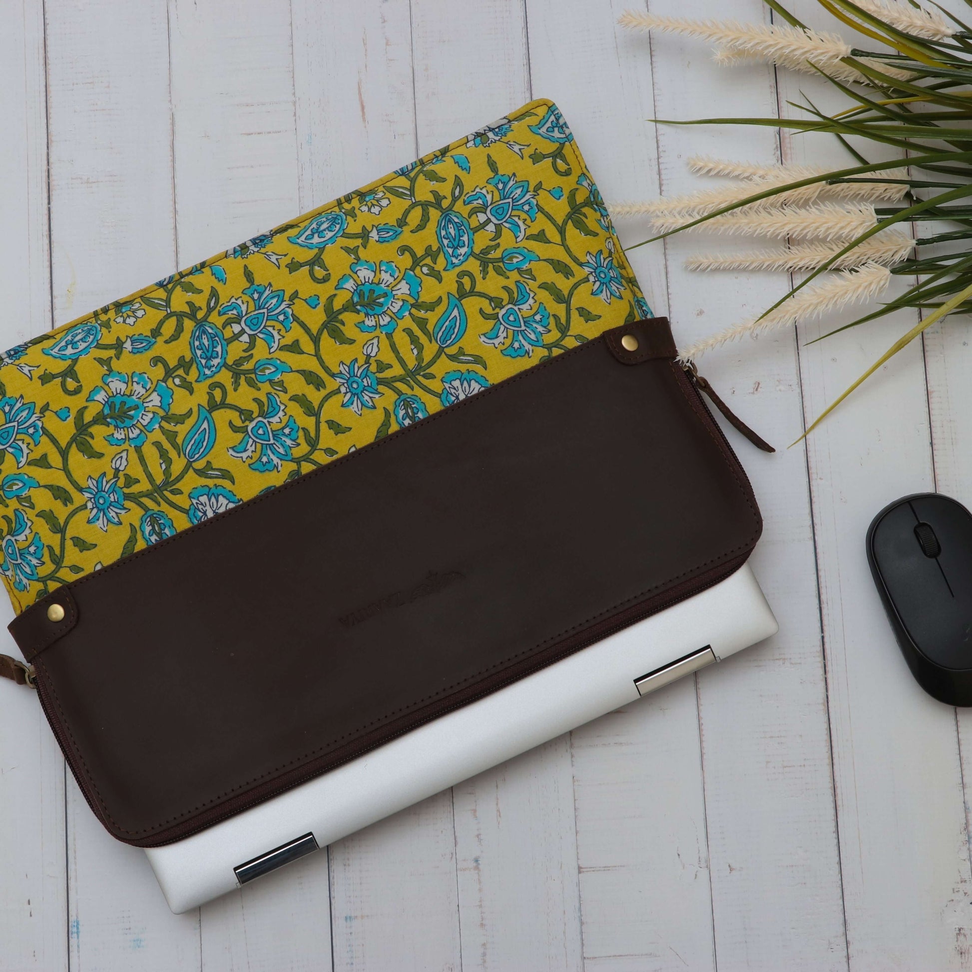 A leather laptop sleeve with a yellow floral block print on the lower half with Black mouse on the otherside.
