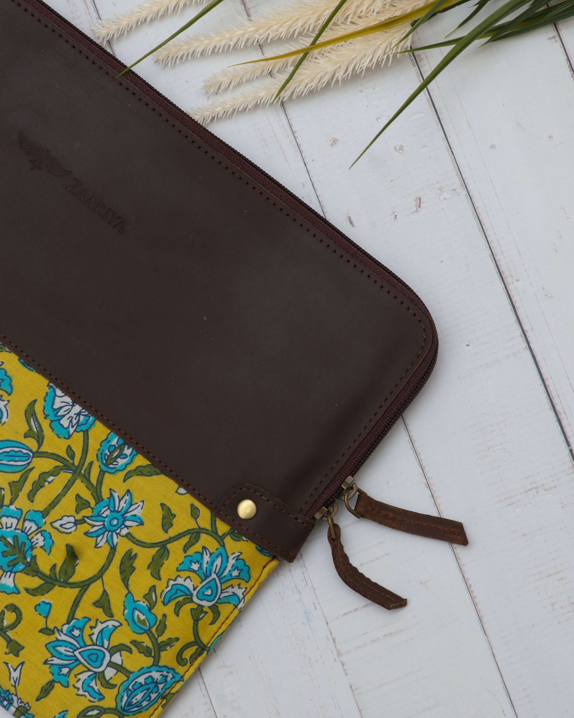 A leather laptop sleeve with a yellow floral block print on the lower half, closeup photo.