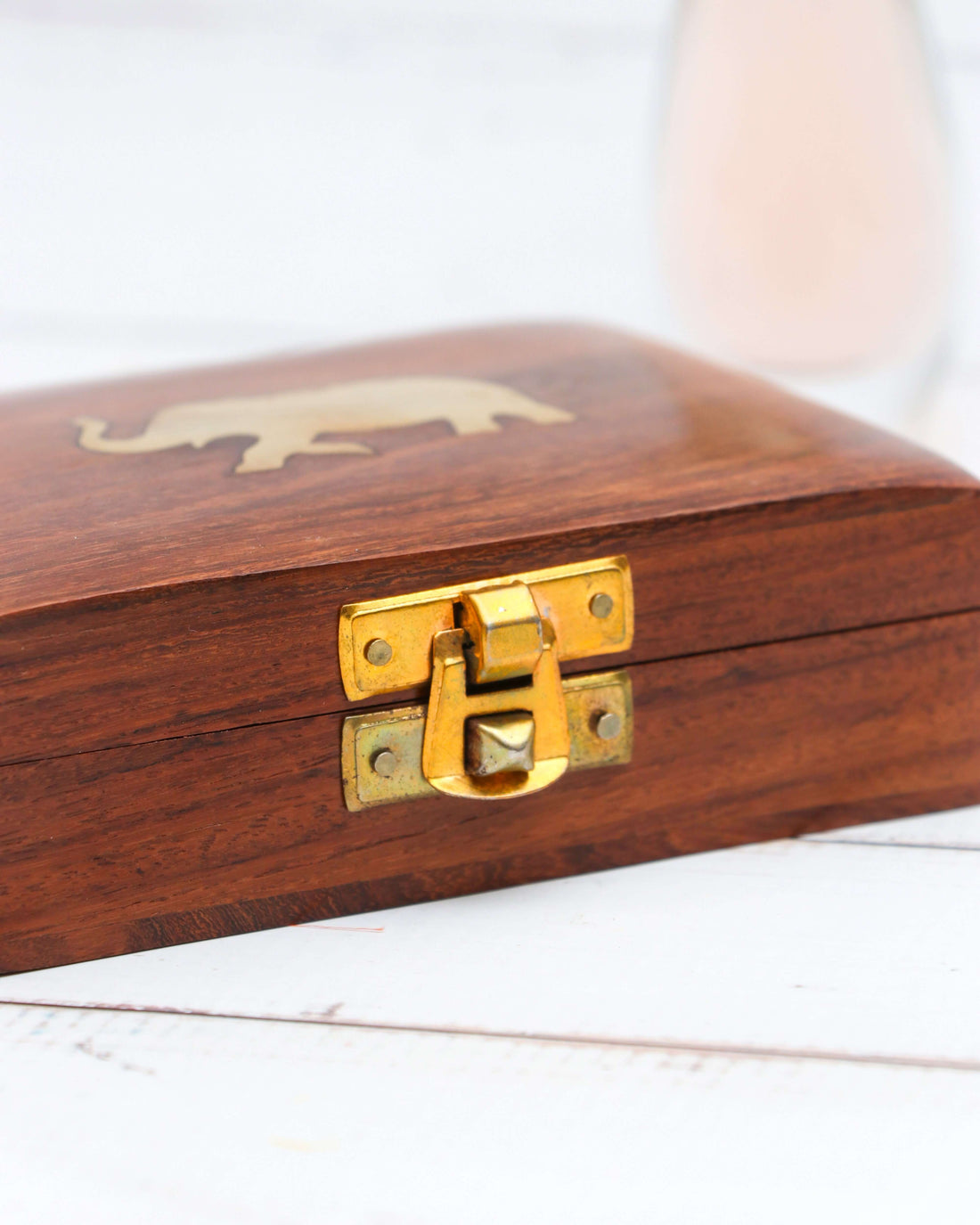 A small, rectangular, handcrafted wooden jewelry box with a brass latch on the front and a brass elephant inlaid on the lid. The wood has a natural grain and a polished finish.