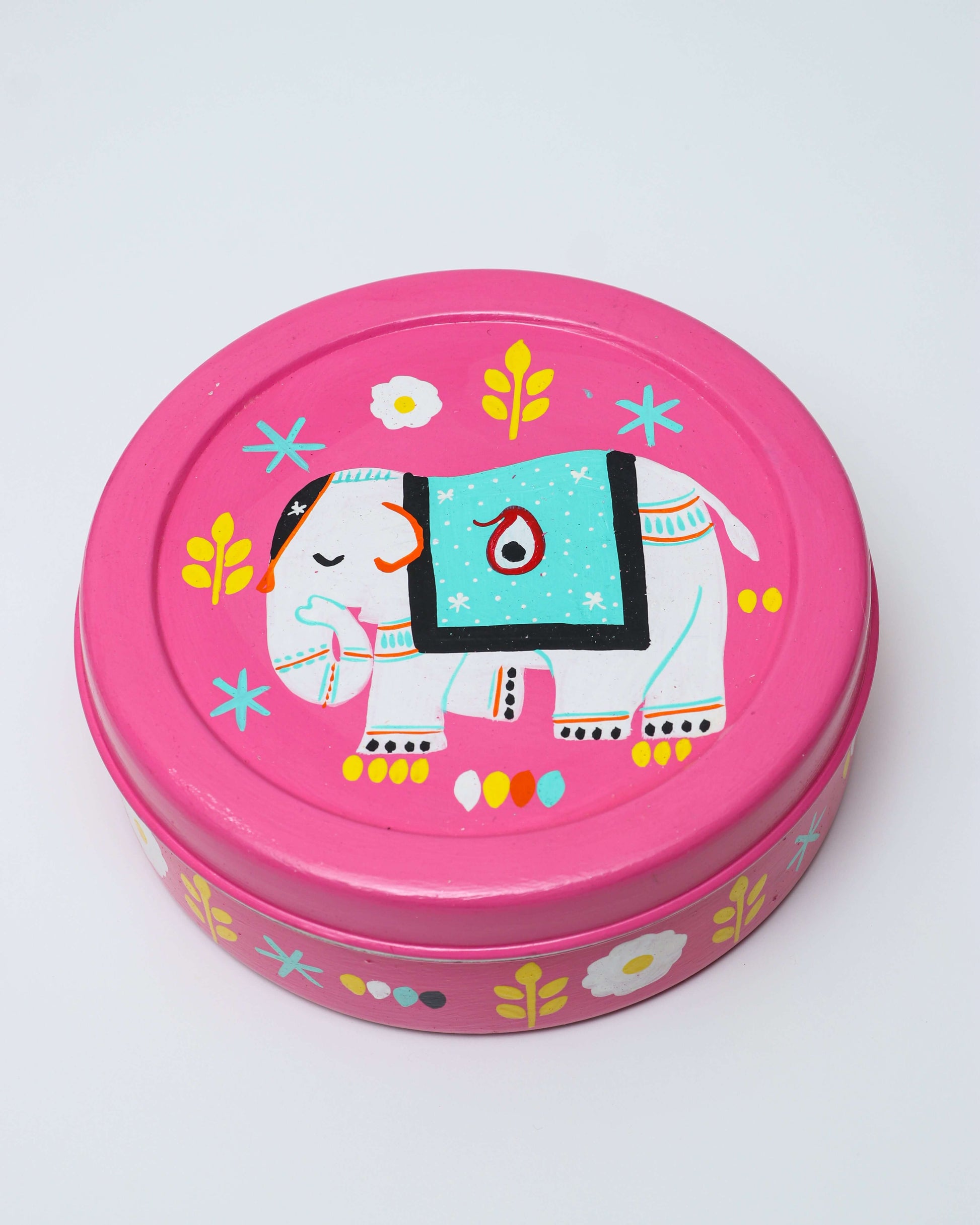 A pink, round hand-painted steel spice box featuring a white elephant with a turquoise-colored blanket on its back. The design also includes yellow leaves, white flowers, and small dot patterns.