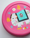 A close-up of a round, pink hand-painted steel spice box lid. The lid features a central illustration of a white elephant with its trunk raised. The elephant is adorned with a turquoise blanket patterned with white dots, yellow leaves, and white flowers.