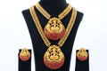 A Traditional Long Temple Necklace set with Laxmi Pendants is shown, featuring a gold-toned two-piece necklace with intricate chains and matching earrings. Each piece has a large, central pendant depicting the goddess Laxmi surrounded by ruby-red beads. The jewelry is displayed on a black mannequin bust.