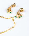 A pair of intricate earrings and a section of a chain from a Gold Temple Jewellery Necklace are displayed on a white background. The gold-toned earrings feature a stylized peacock or elephant head design, embellished with clear and red stones. Dangling from the earrings are clusters of white pearls and green beads. A simple gold chain is visible in the foreground.