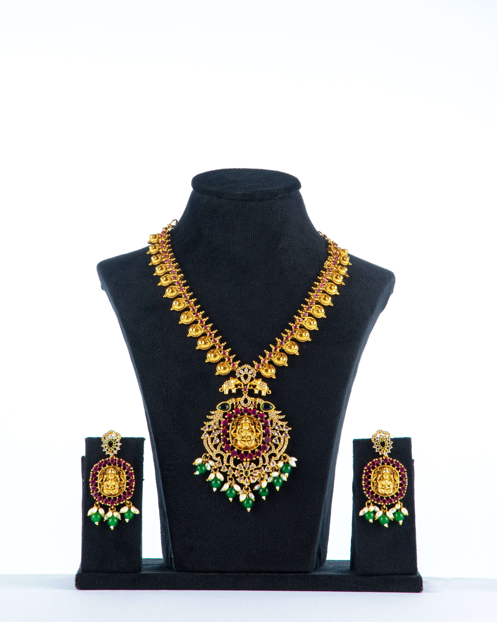 A South Indian coin necklace with a Goddess Laxmi pendant displayed on a mannequin bust, accompanied by a pair of matching earrings.