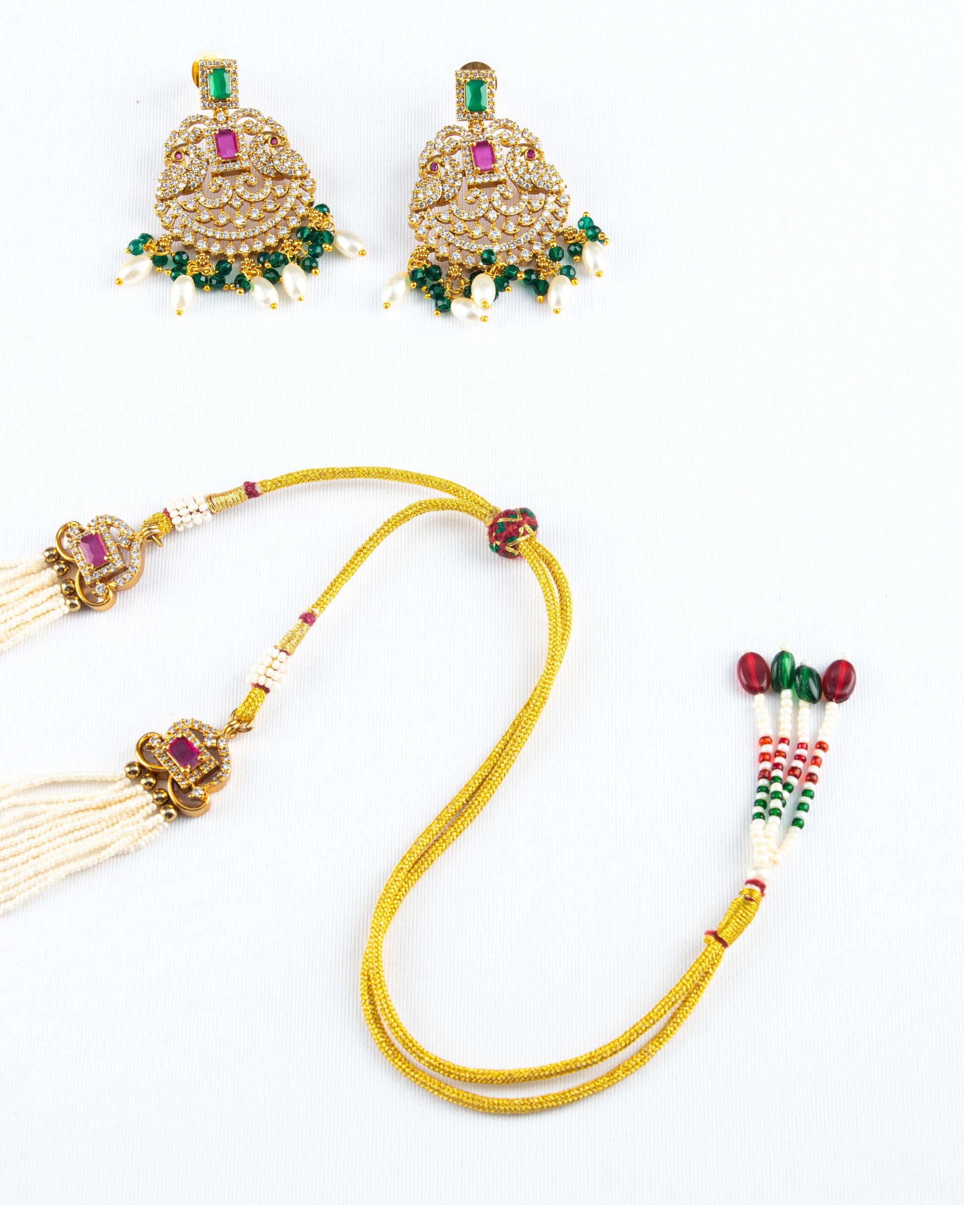 A pair of traditional gold-toned earrings with clear and red stones and green and white bead drops, along with a matching adjustable necklace cord featuring pearl tassels and decorative red and green beads.