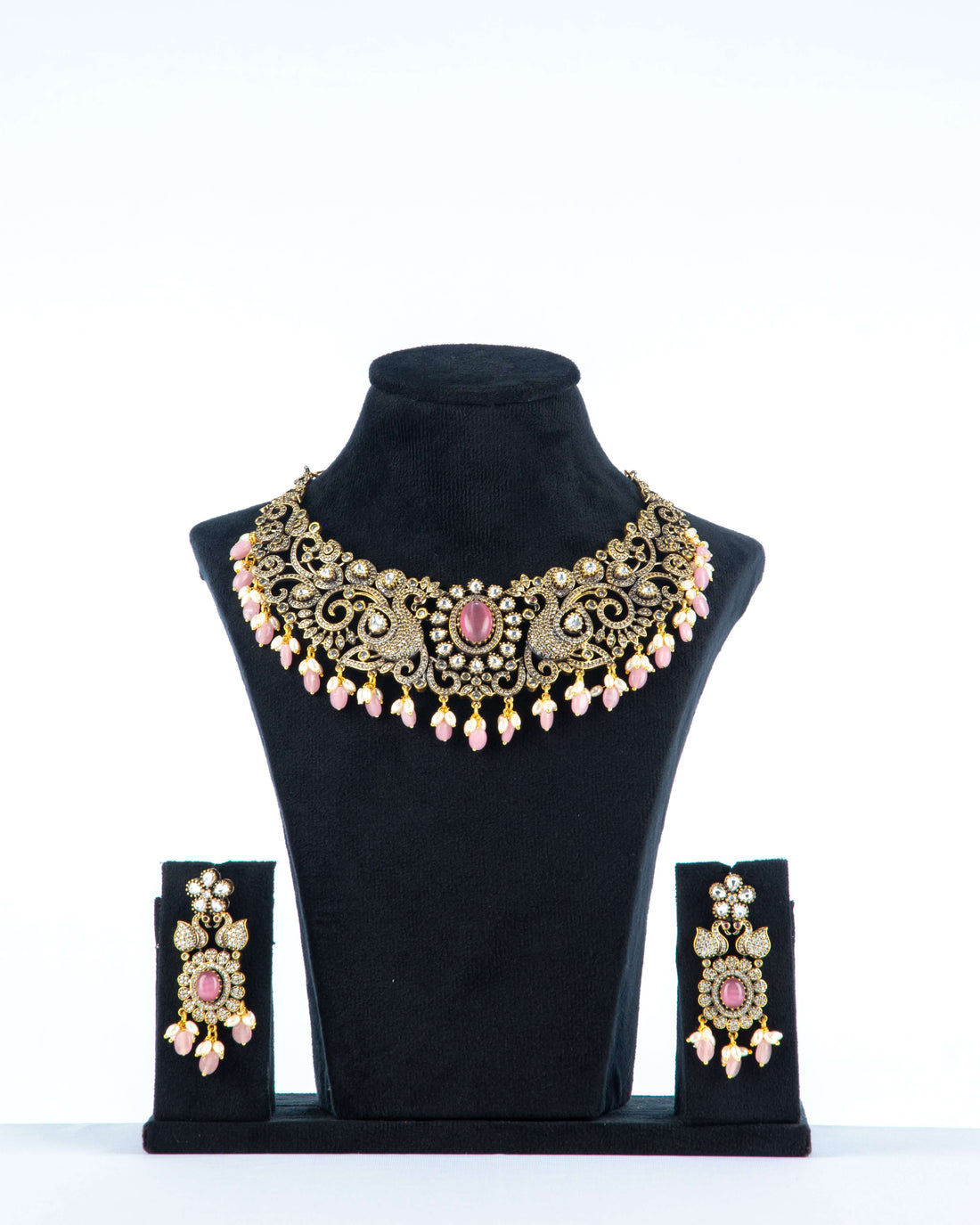 A Victorian-style necklace in pastel pink with intricate details, displayed on a mannequin bust. The necklace is adorned with beads, pearls, and a central pendant.