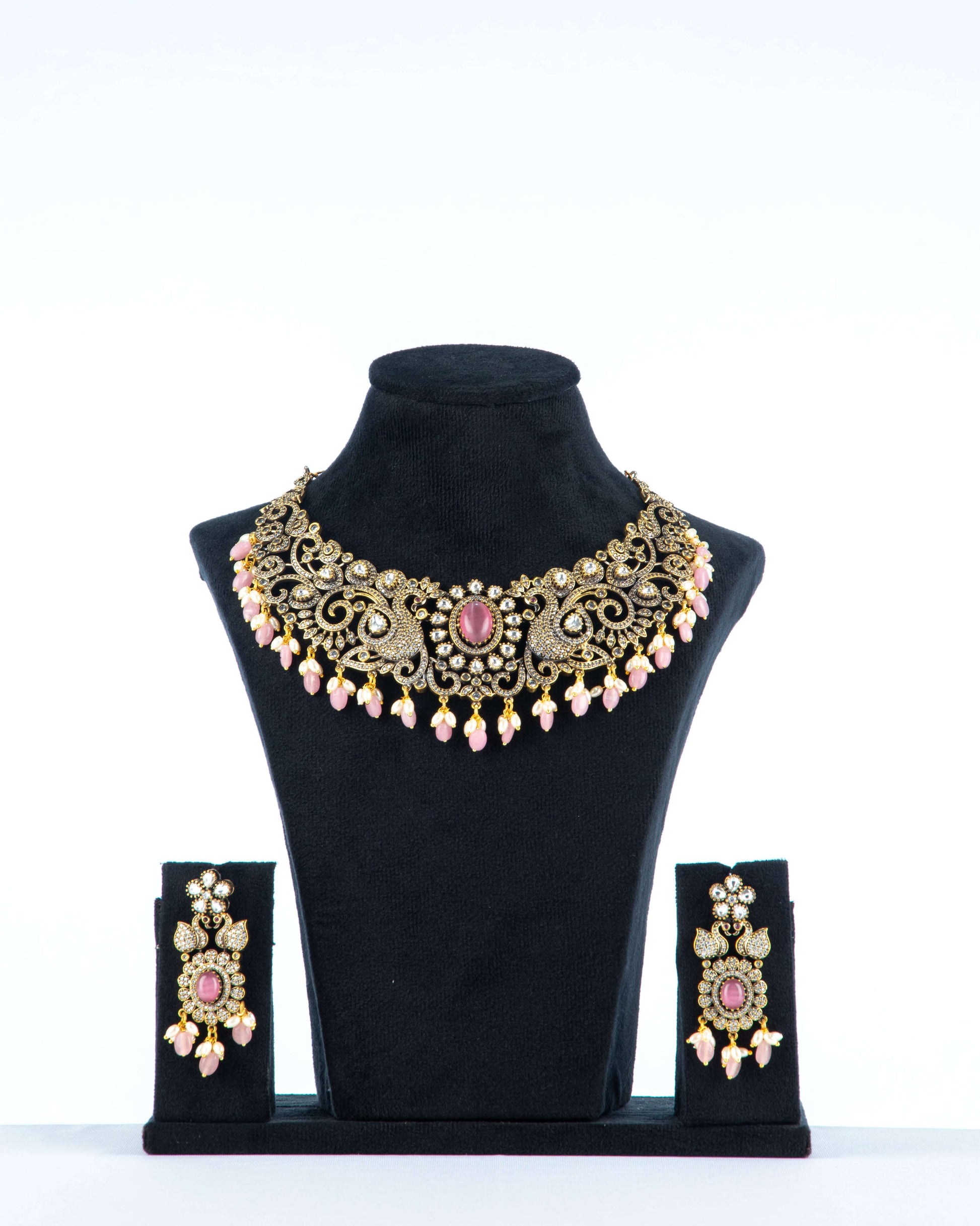 A Victorian-style necklace in pastel pink with intricate details, displayed on a mannequin bust. The necklace is adorned with beads, pearls, and a central pendant.