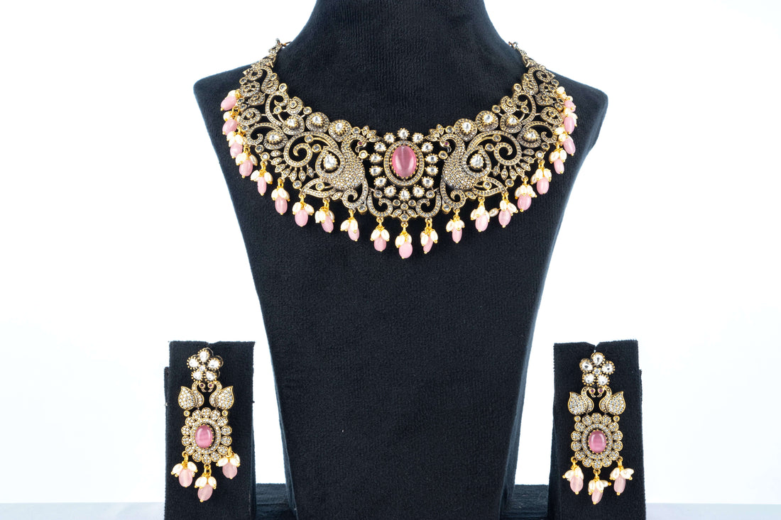 A Victorian-style necklace in pastel pink with intricate details, displayed on a mannequin bust. The necklace is adorned with beads, pearls, and a central pendant.