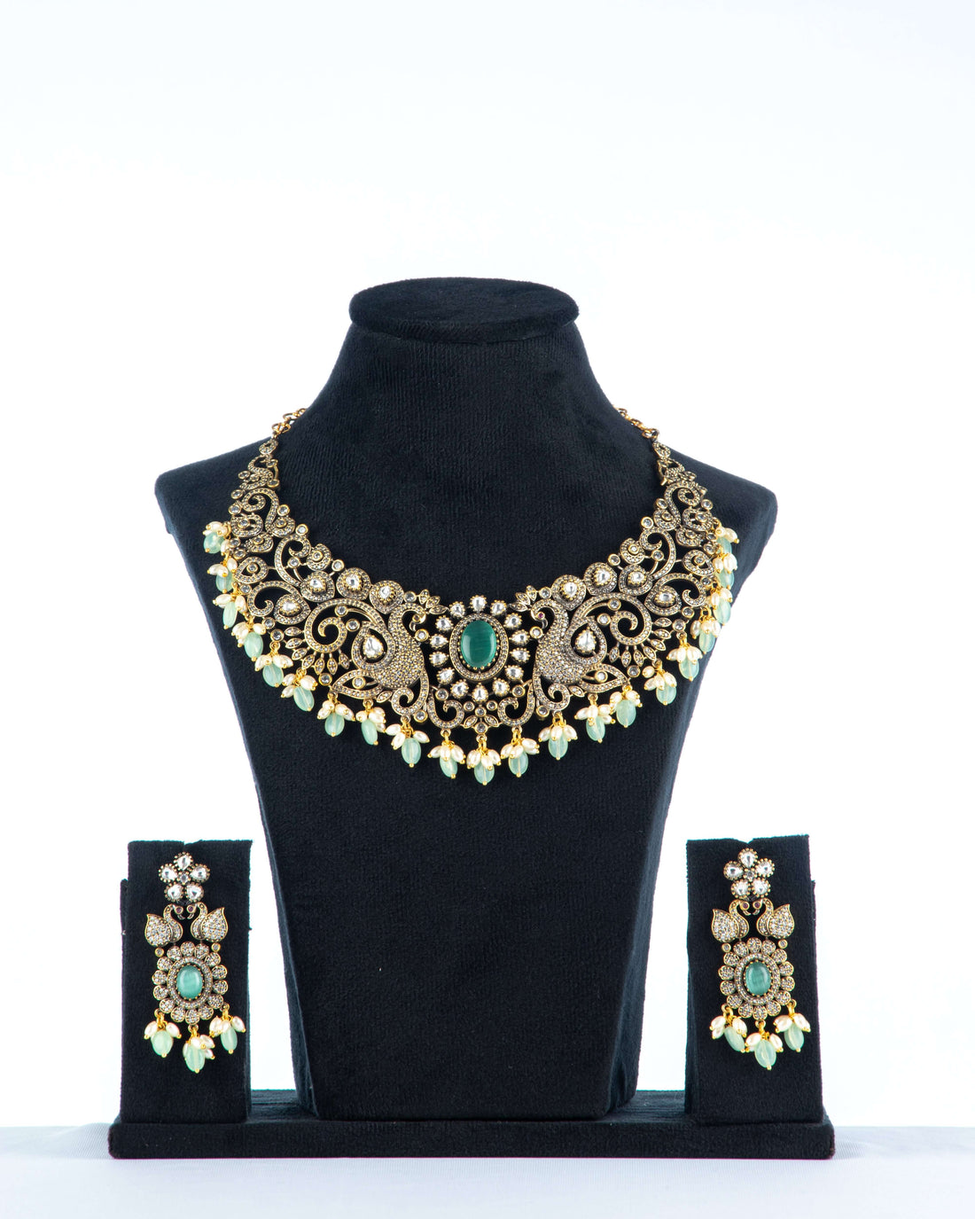 A Victorian-style beaded necklace with a black pendant, featuring vibrant green beads and intricate gold detailing, displayed on a mannequin bust.