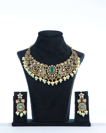 A Victorian-style beaded necklace with a black pendant, featuring vibrant green beads and intricate gold detailing, displayed on a mannequin bust.