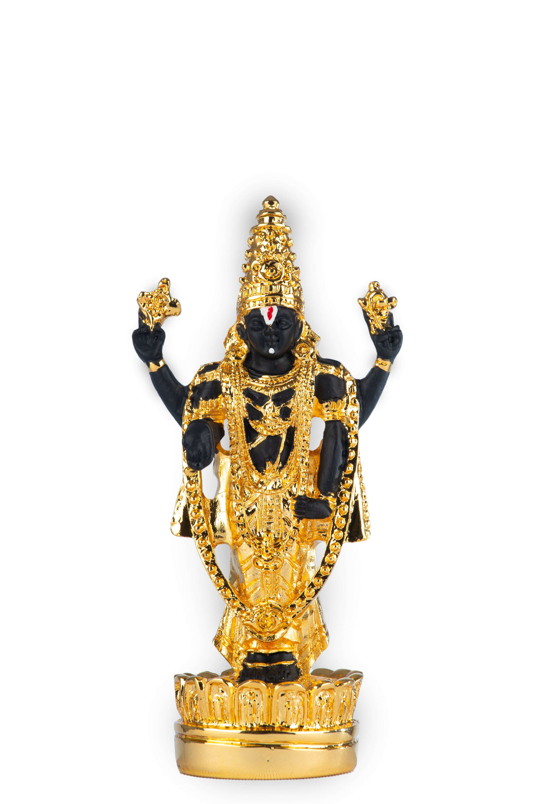 A black idol of Lord Venkateswara (Balaji) adorned with elaborate gold ornaments and a traditional white and red namam on the forehead, standing on a golden base with scattering yellow and orange marigold petals around it, against a blurred background with a lamp.