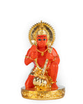 A vibrant orange-red Lord Hanuman Statue is shown kneeling on a golden, ornate base. The deity holds a golden mace (gada) in one hand and raises the other in a gesture of blessing. The statue is adorned with a golden crown and ornaments and is surrounded by a golden halo.