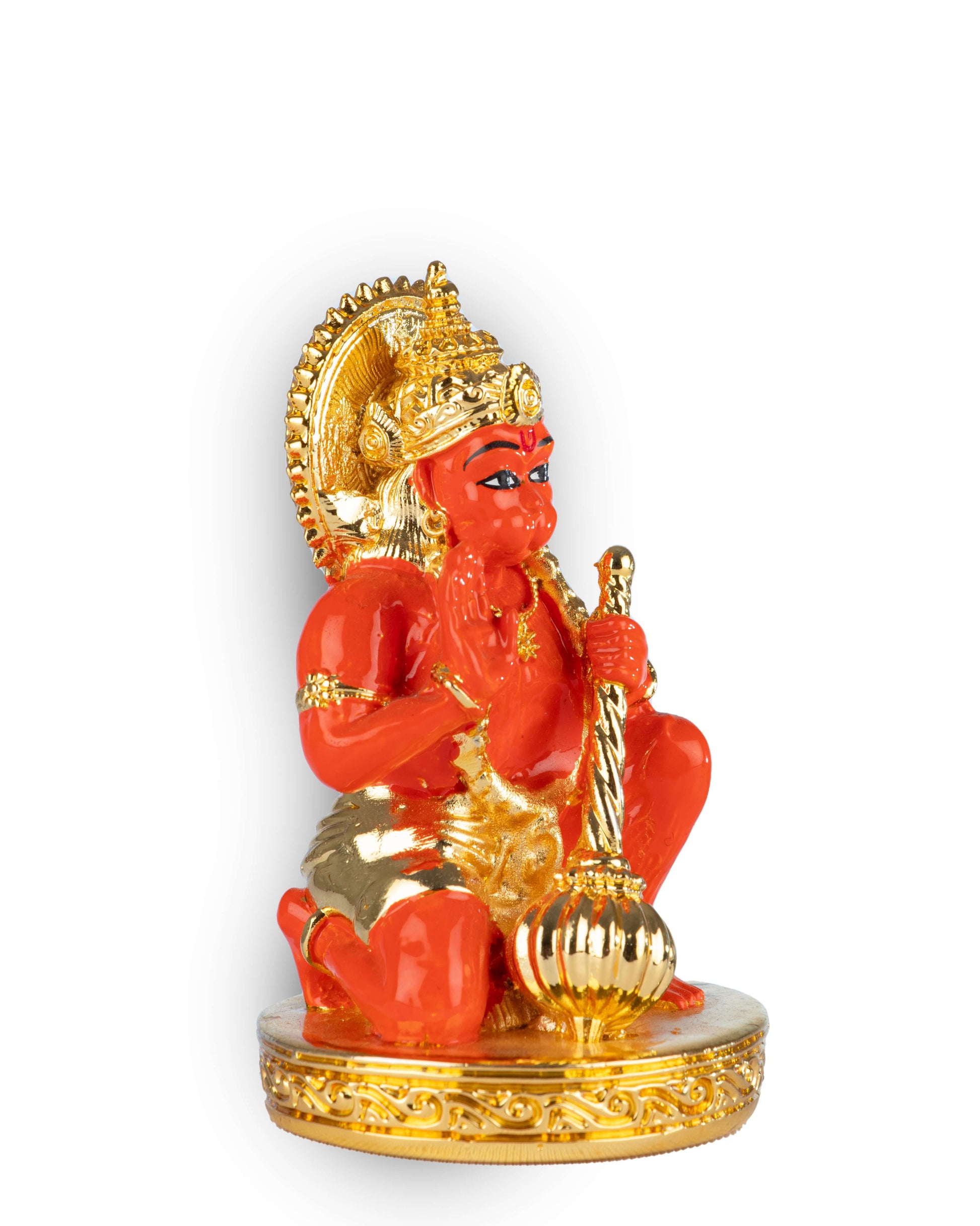A vibrant orange-red and gold statue of a deity, likely Lord Hanuman, is shown kneeling on a golden, ornate base. The deity is holding a golden mace (gada) in one hand and raising the other in a gesture of blessing. The statue is adorned with a golden crown and ornaments and is surrounded by a golden halo.