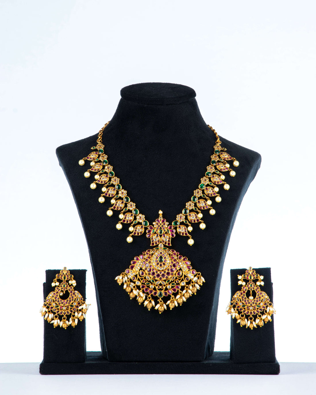 A multi-color polki necklace set with gold plating, pearls, and intricate designs displayed on a black mannequin bust with a pair of matching earrings.
