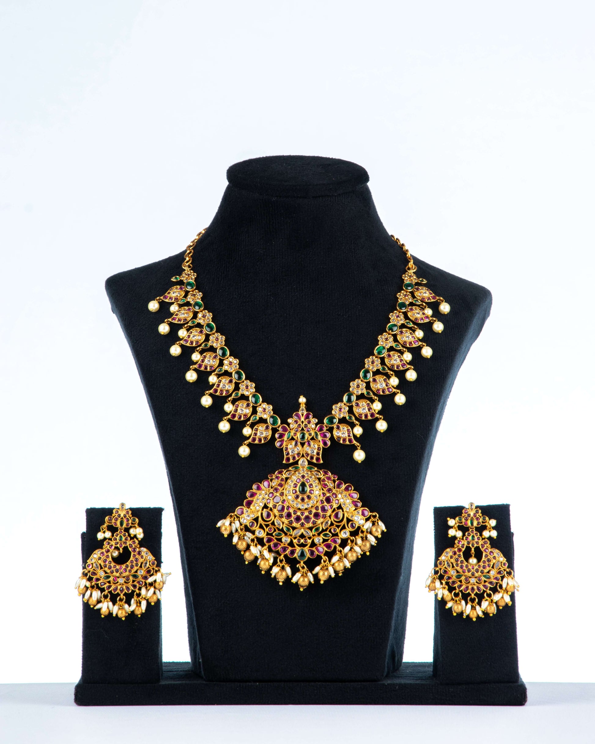 A multi-color polki necklace set with gold plating, pearls, and intricate designs displayed on a black mannequin bust with a pair of matching earrings.