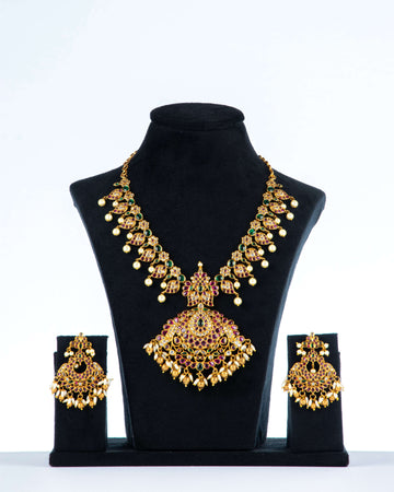 A multi-color polki necklace set with gold plating, pearls, and intricate designs displayed on a black mannequin bust with a pair of matching earrings.